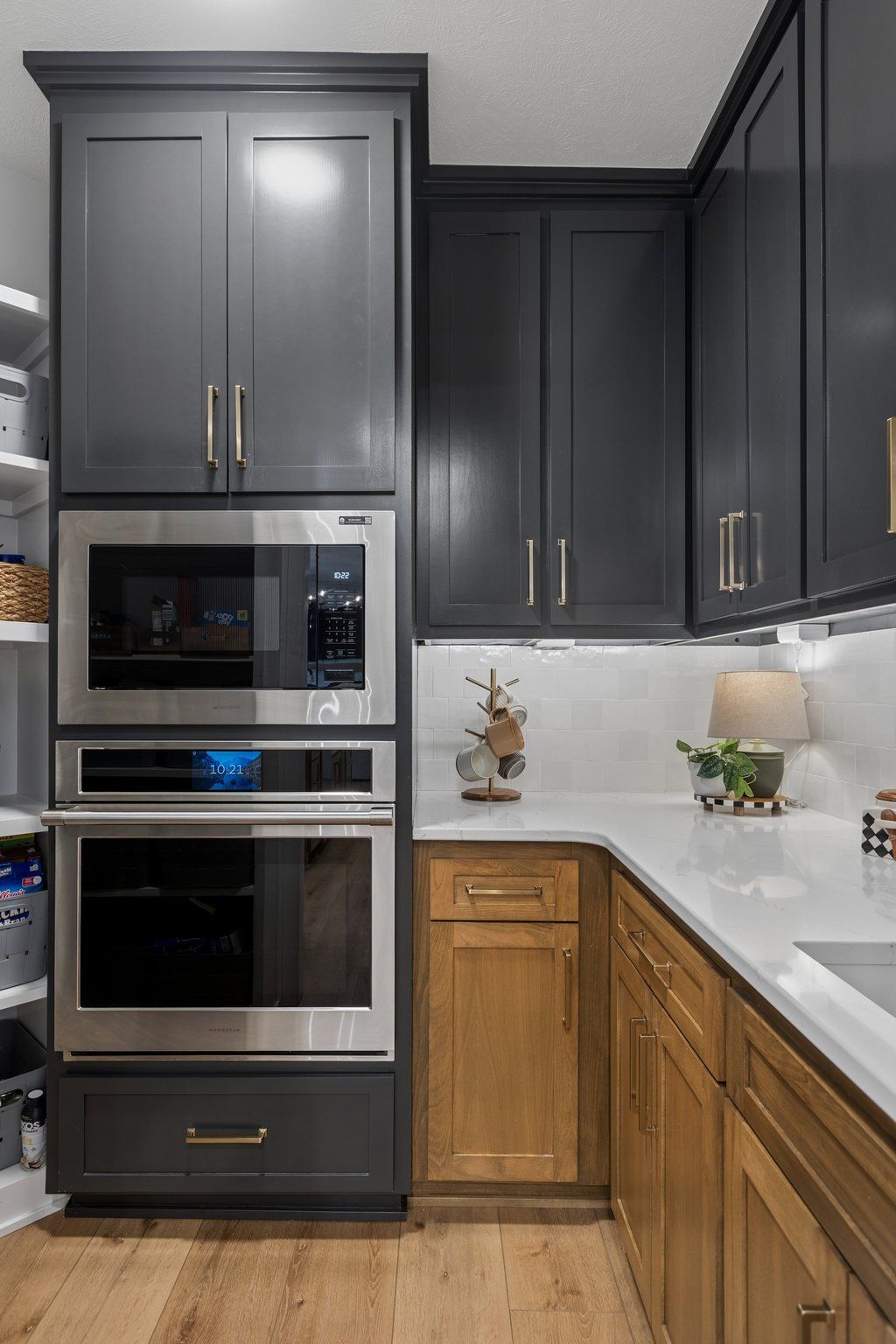 Modern kitchen with dark cabinets, built-in ovens, white countertops, and wood lower cabinets