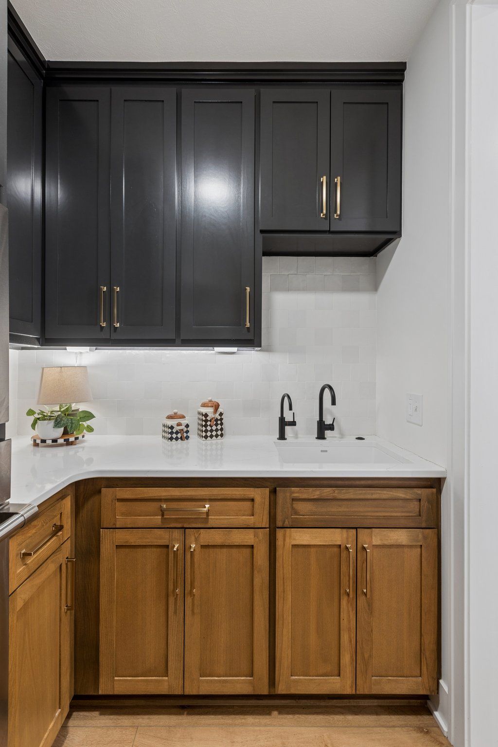 Modern kitchen with dark upper cabinets, natural wood lower cabinets, white countertop, and black faucet.