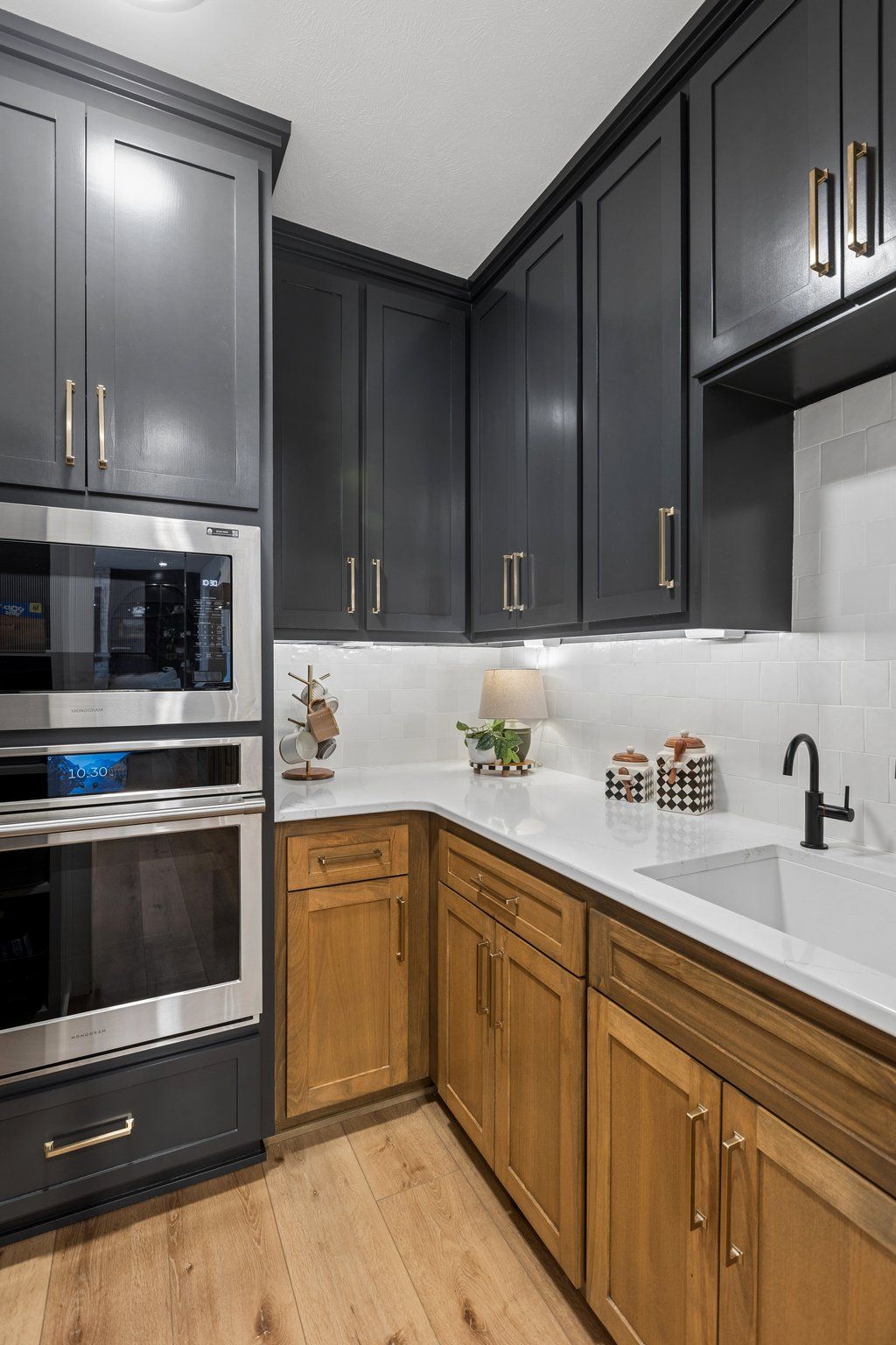 Modern kitchen with dark gray upper cabinets, wood lower cabinets, white countertop, and built-in stainless ovens.