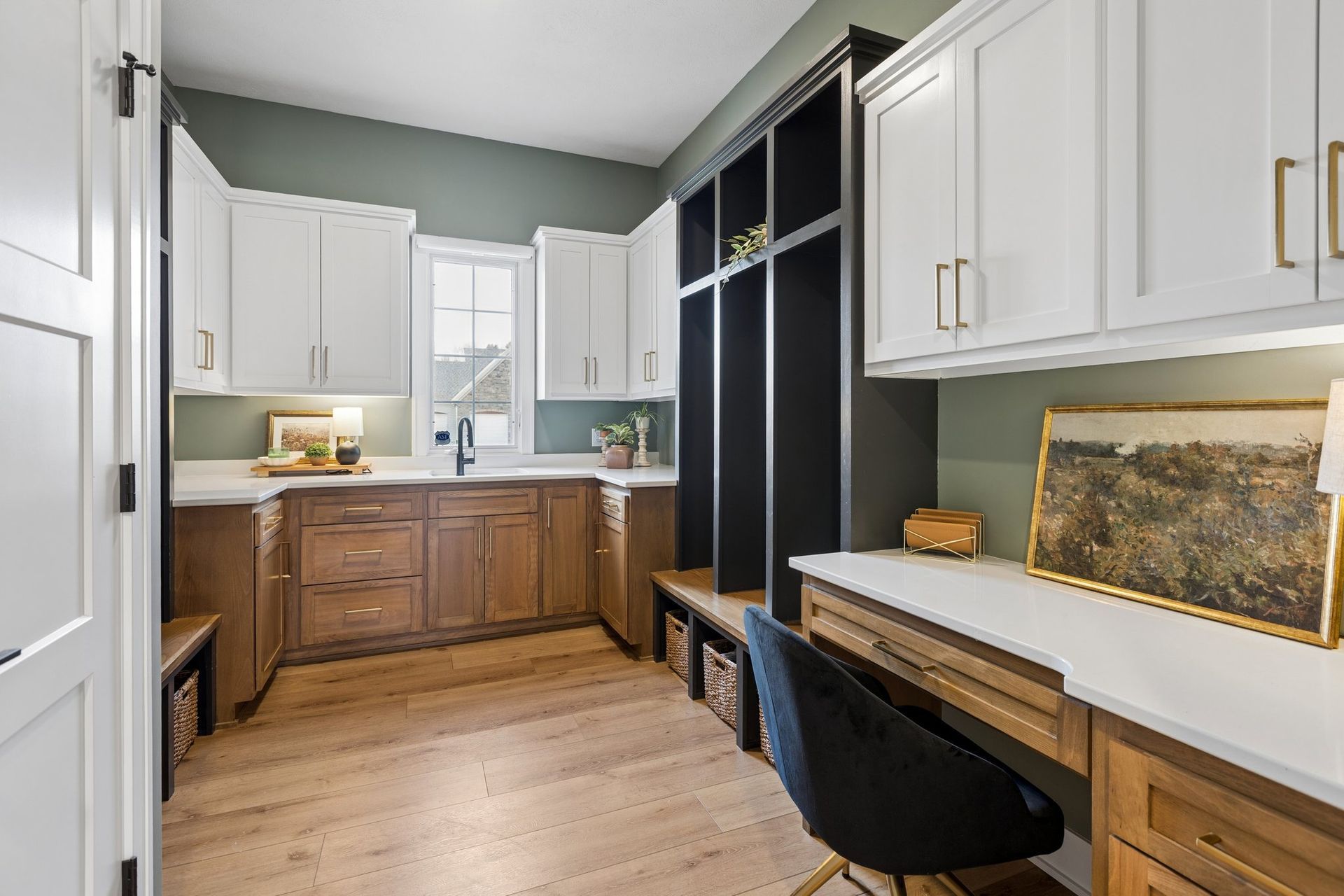 Narrow home office with white cabinets, wood desk, black chairs, and a window at the back