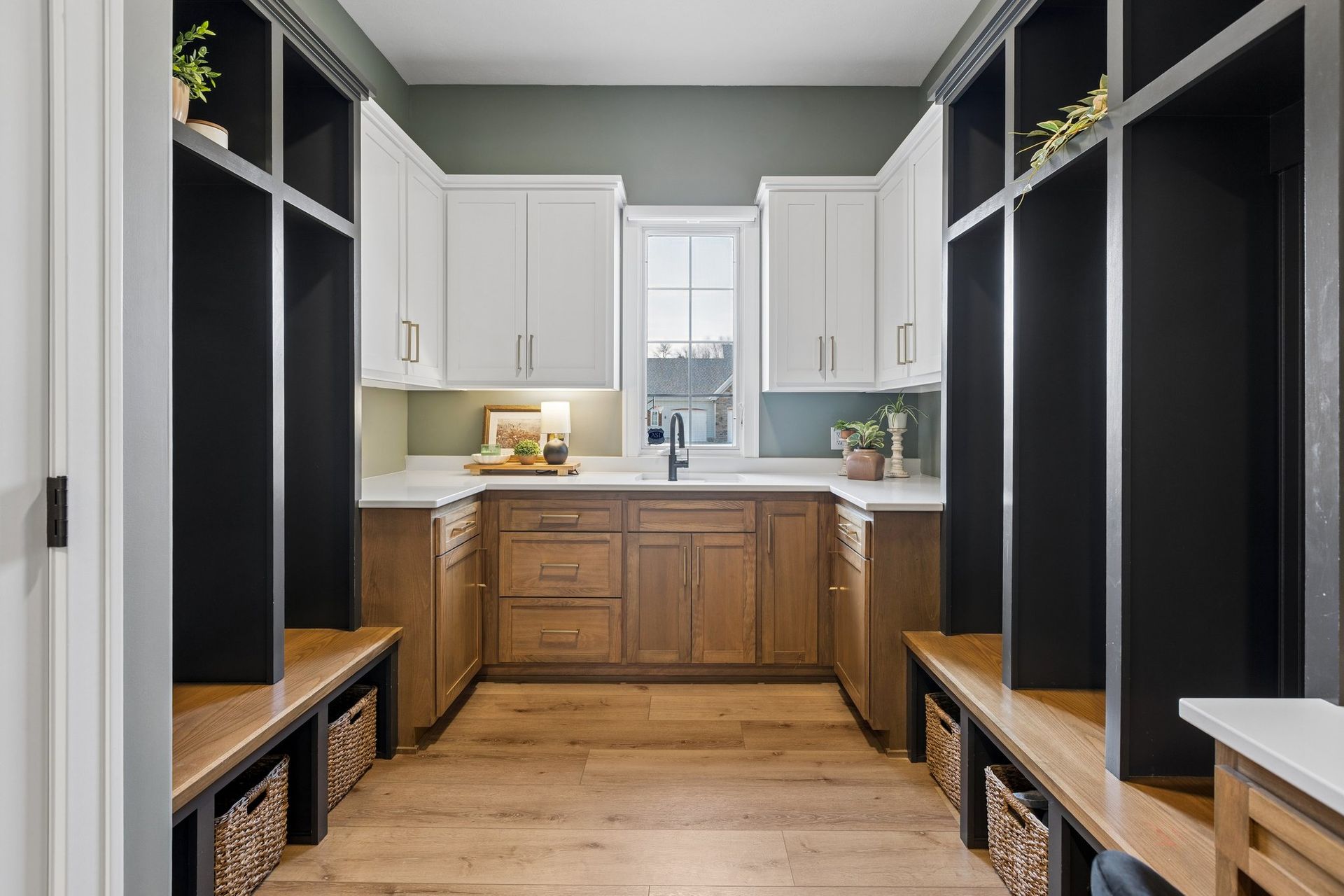 Narrow mudroom with black built-ins, wood benches, and white cabinets leading to a kitchen.