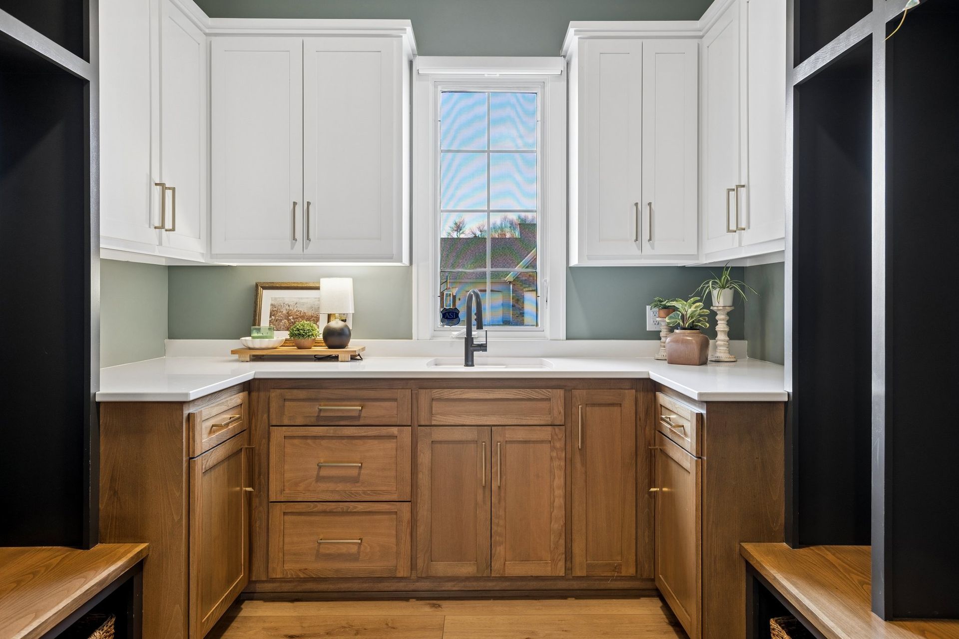 Modern kitchen with white upper cabinets, wood lower cabinets, and a centered window above the sink.