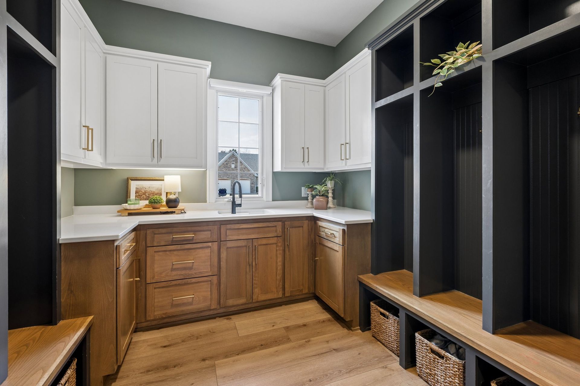 Modern laundry room with white cabinets, wood lower cabinets, black cubbies, and a window over the sink.
