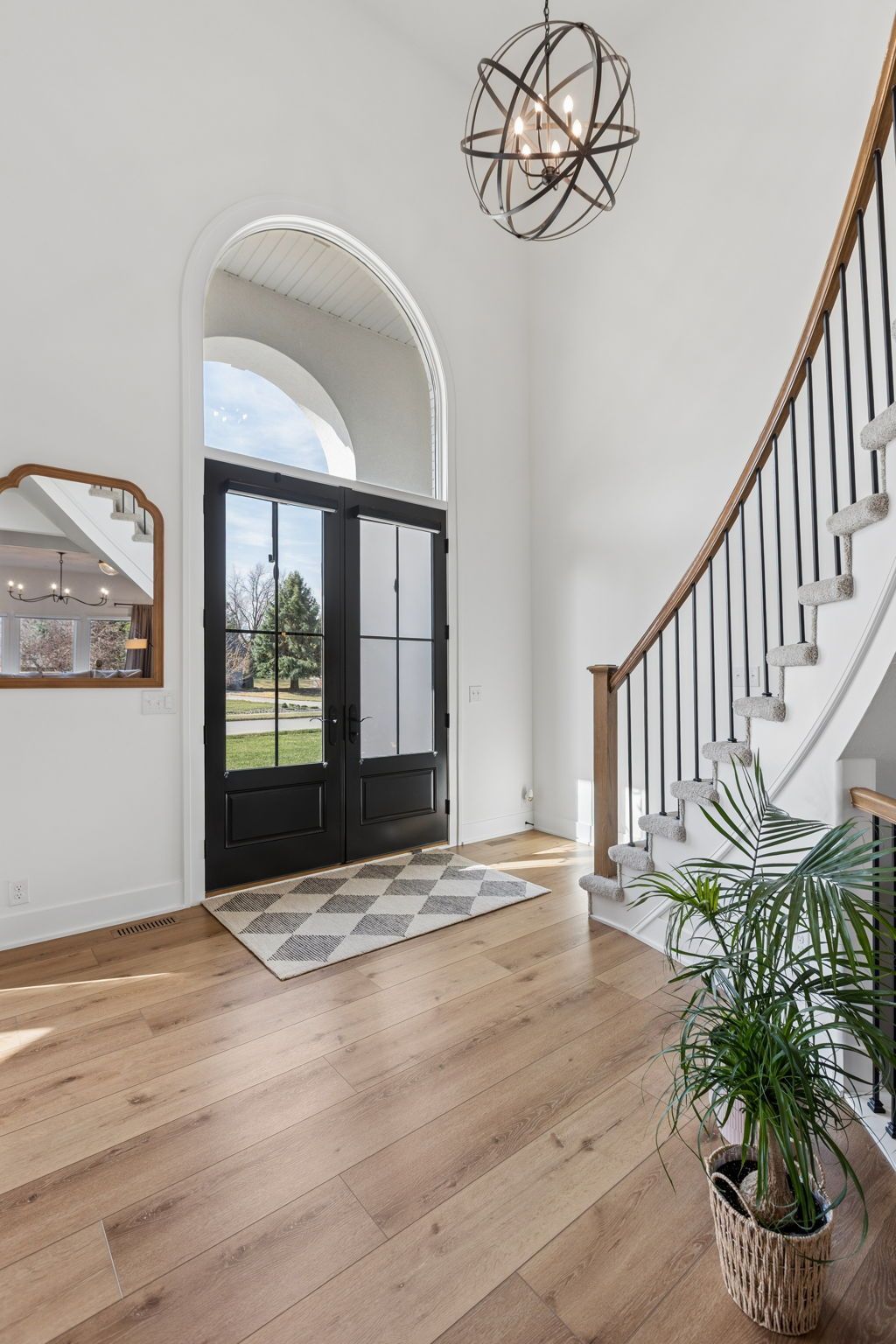 Bright entryway with black front door, curved staircase, wood floors, and potted plant