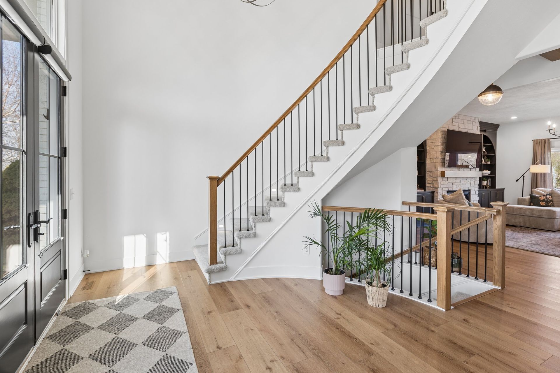 Bright entryway with staircase, hardwood floors, and potted plants beside a dining area