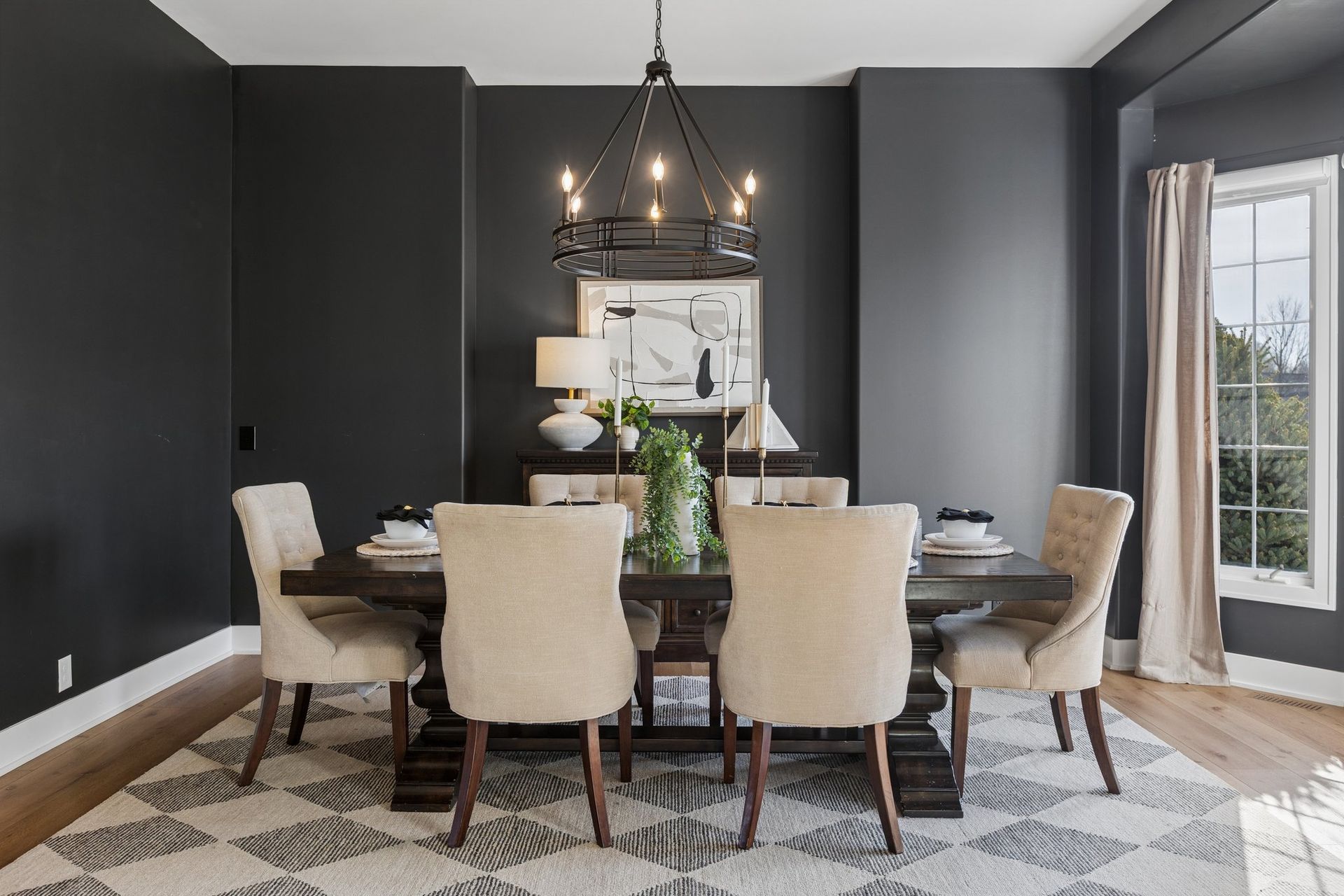 Modern dining room with dark walls, beige chairs, a chandelier, and a patterned rug