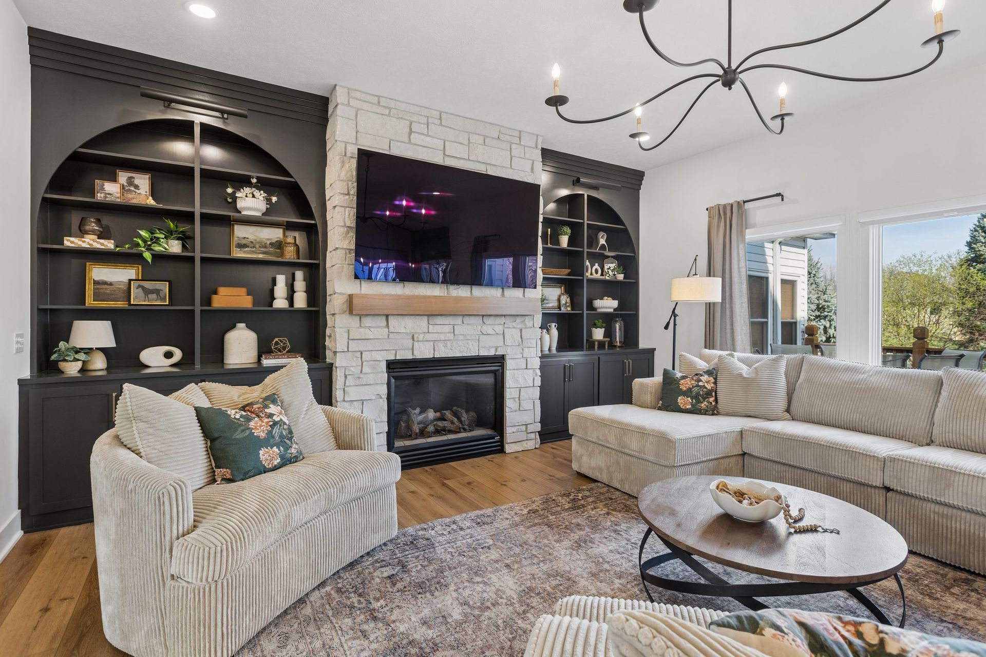 Bright living room with gray sectional, fireplace, built-in shelves, and large TV above the mantel.