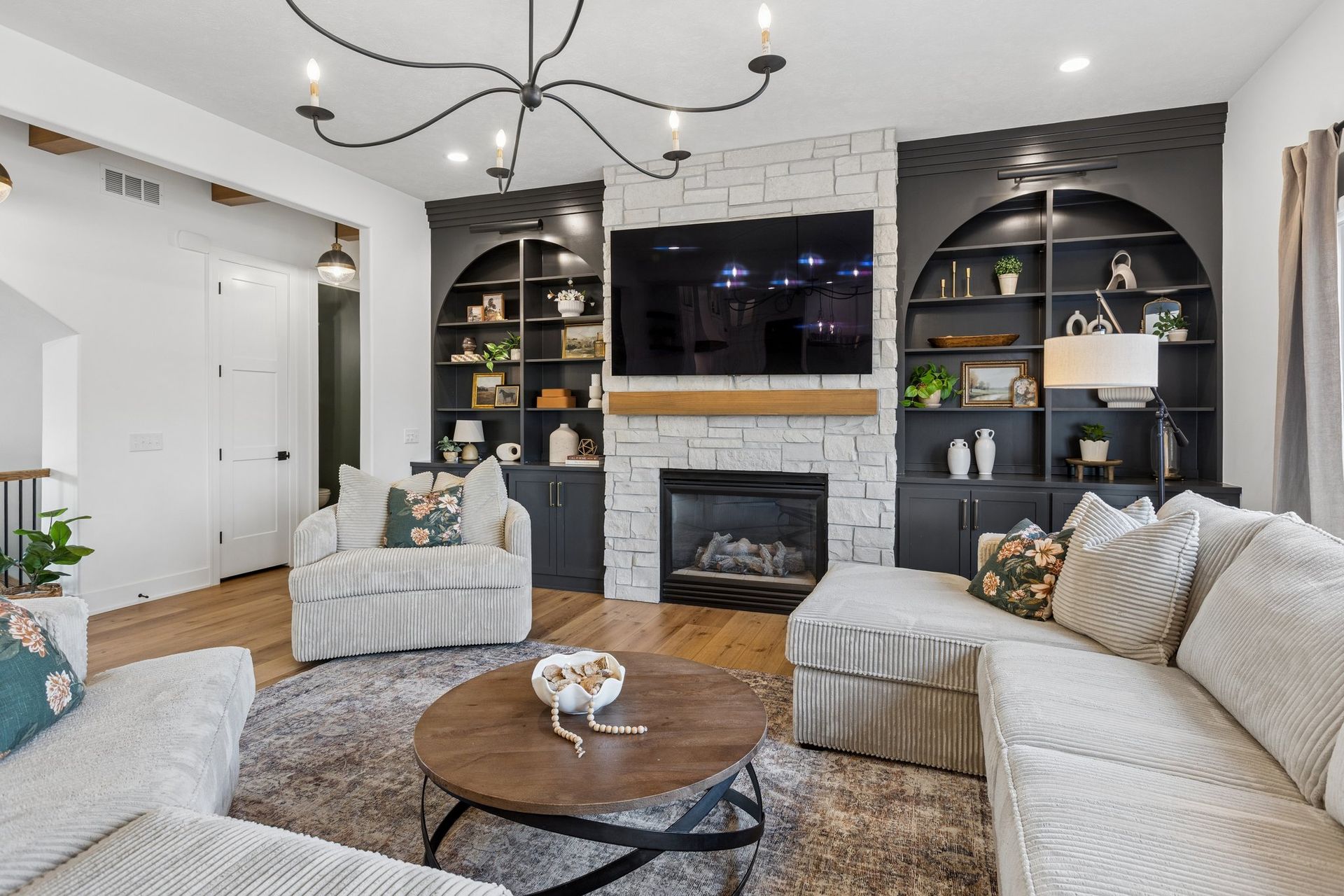 Bright living room with white sofas, round wood coffee table, fireplace, and built-in black shelves