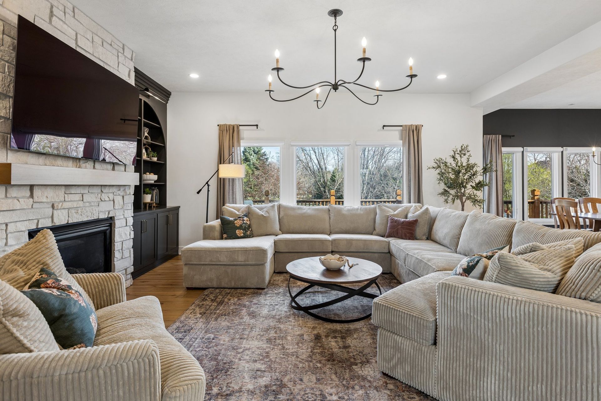 Spacious modern living room with beige sectional seating, fireplace, large TV, and chandelier