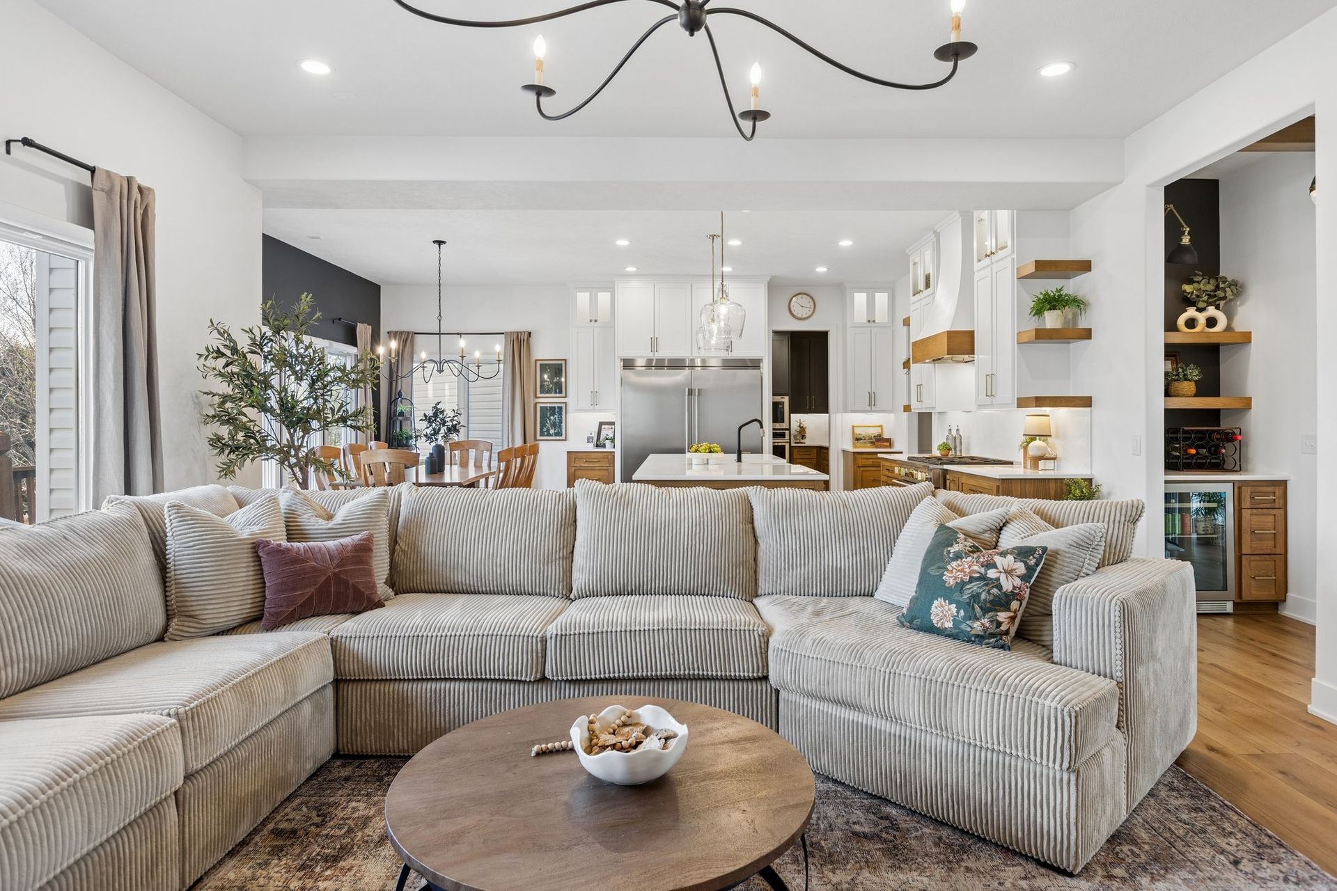 Bright modern living room with a large sectional sofa, round coffee table, and open kitchen in the background