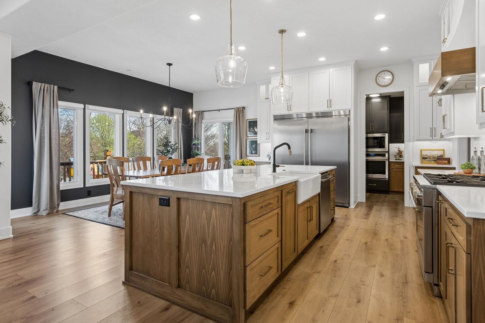 Modern kitchen with large island, stainless appliances, wood floors, and dining area by windows