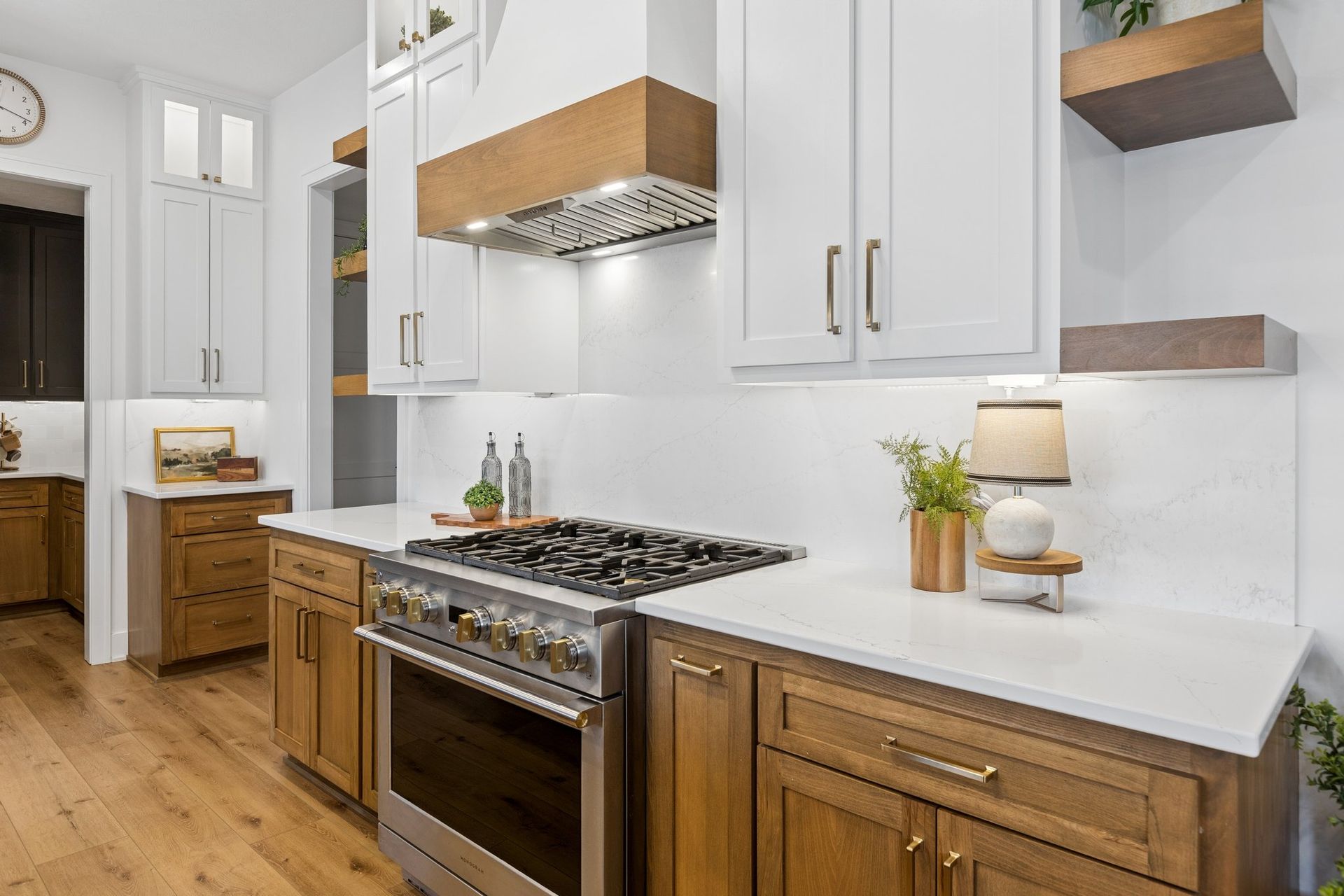 Bright modern kitchen with white cabinets, wood lower cabinets, stainless stove, and white countertops