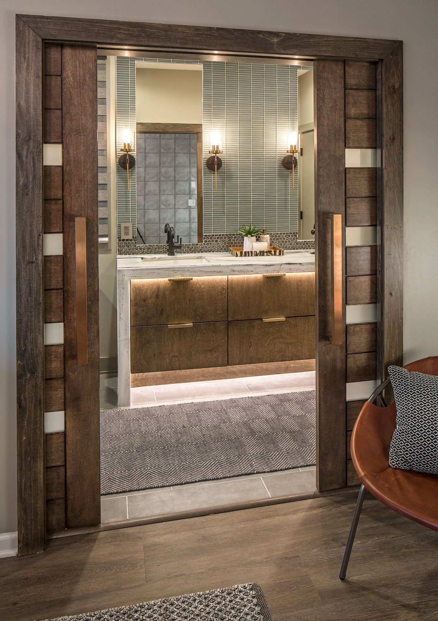 Framed doorway to a bathroom vanity with mirror, wood cabinets, and woven floor mat