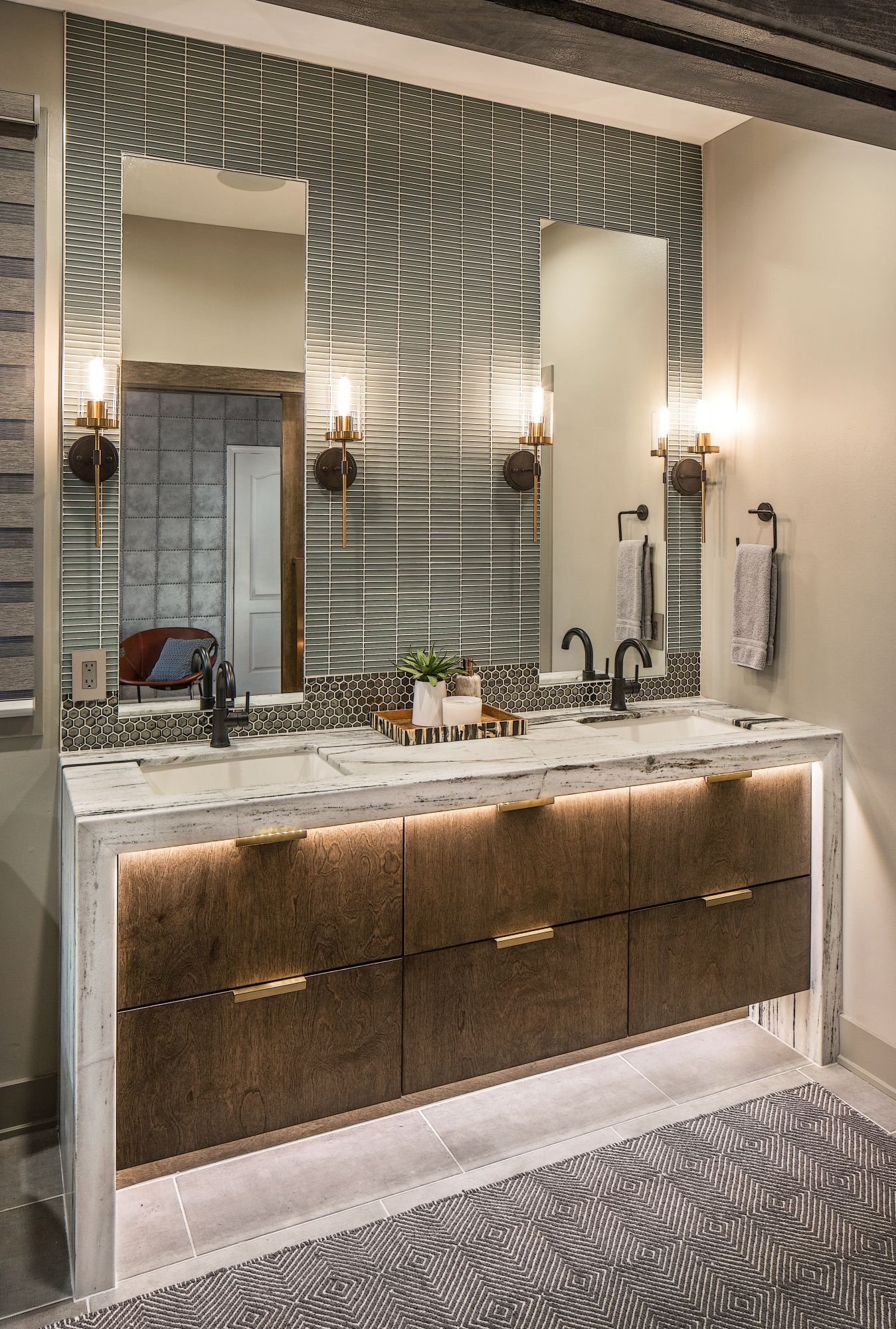 Modern bathroom vanity with marble countertop, large mirrors, wall sconces, and patterned tile walls and floor