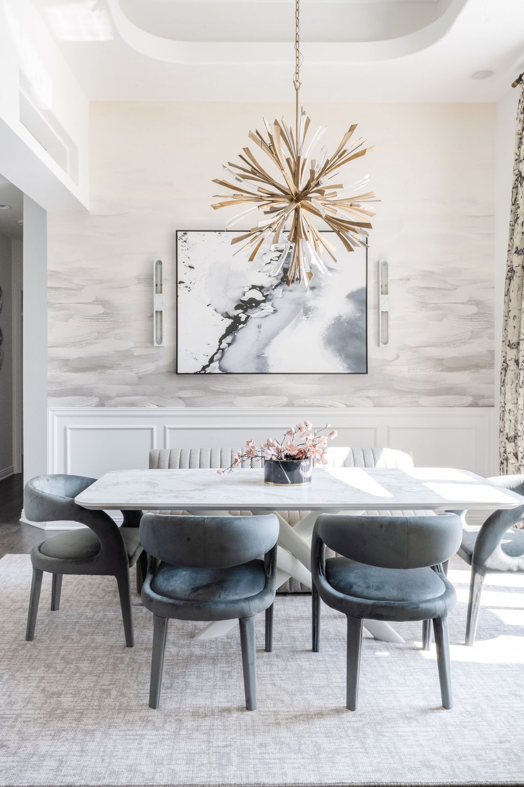 Elegant dining room with gold chandelier, abstract wall art, and gray upholstered chairs around a white table