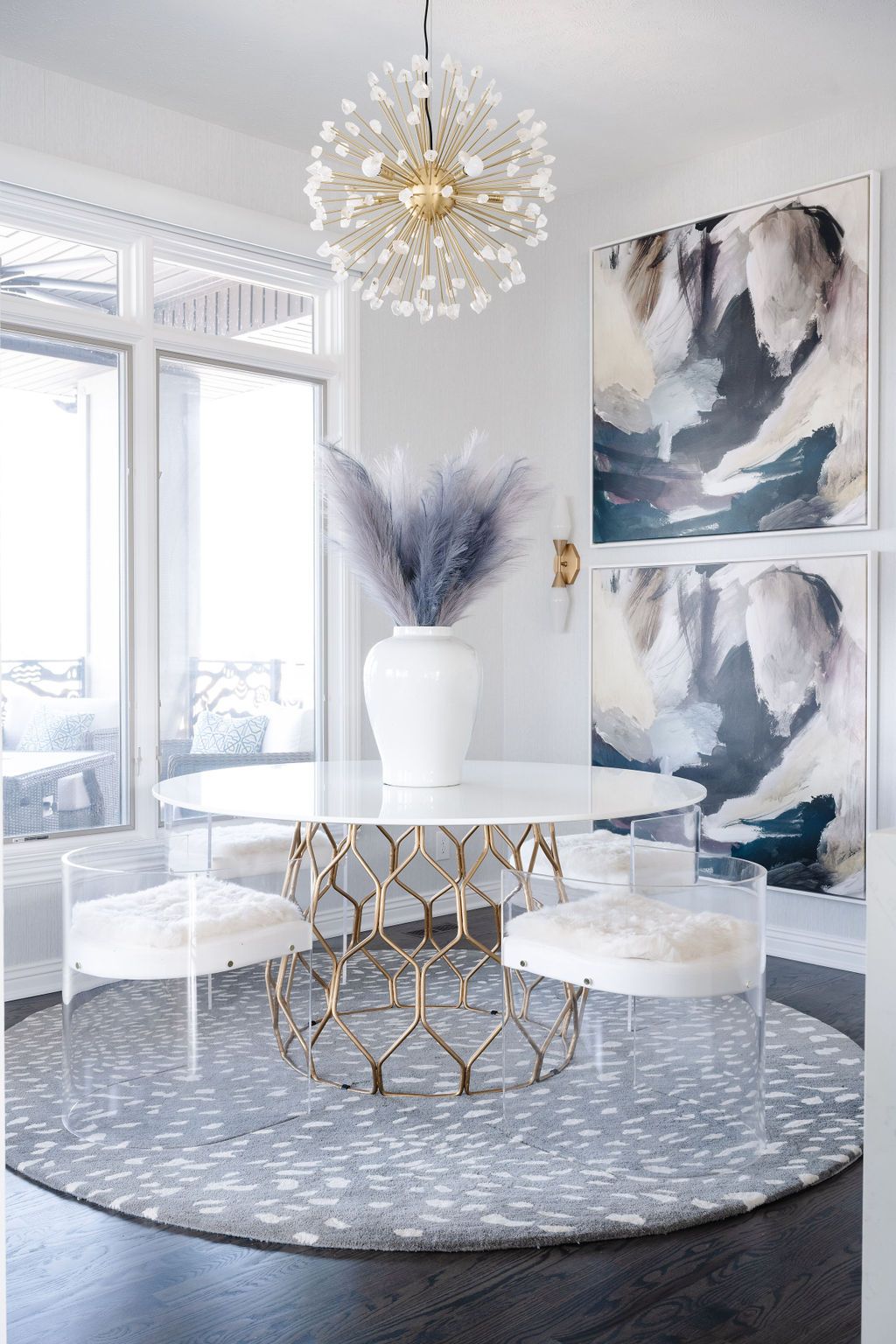 Elegant white dining nook with gold chandelier, round table, abstract art, and blue patterned rug
