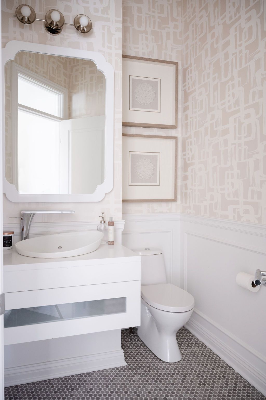 Small bathroom with white vanity, ornate mirror, toilet, and patterned wallpaper.