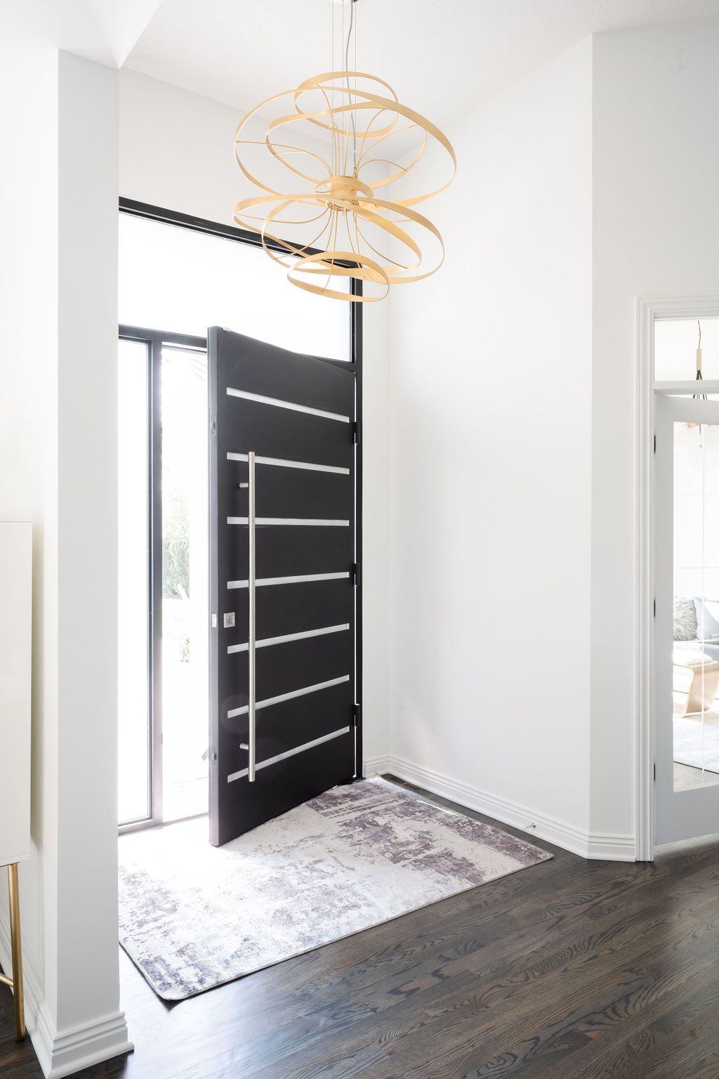 Modern entryway with open black front door, gold pendant light, white walls, and dark wood floor