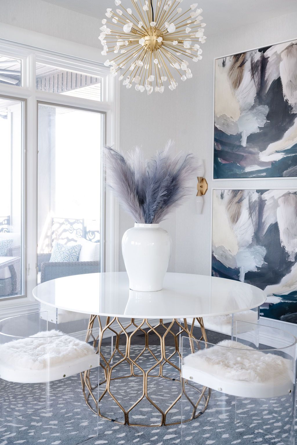 Modern dining nook with a round white table, furry stools, abstract art, and a gold chandelier