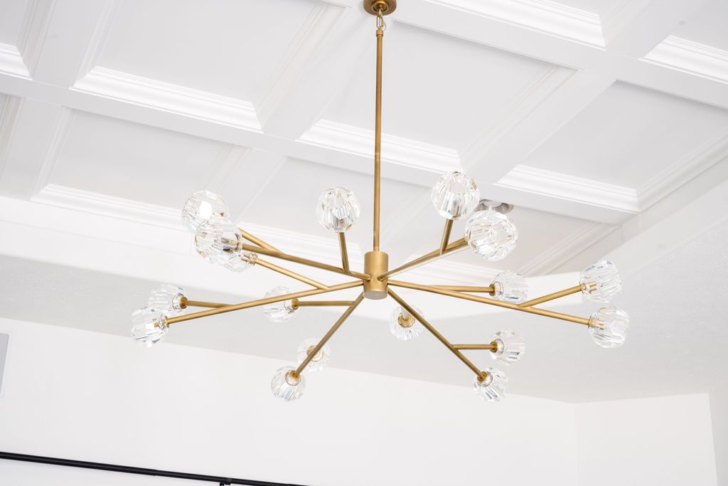 Gold chandelier hanging from a white coffered ceiling in a bright room
