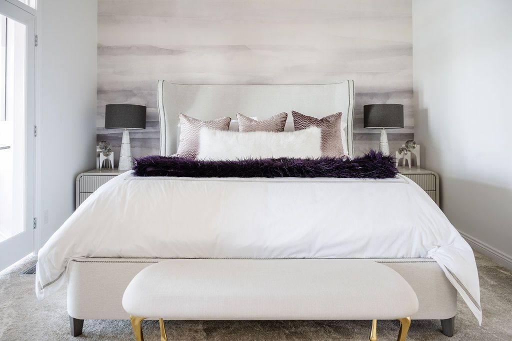 Bright white bedroom with a neatly made bed, gray accents, and a bench at the foot of the bed