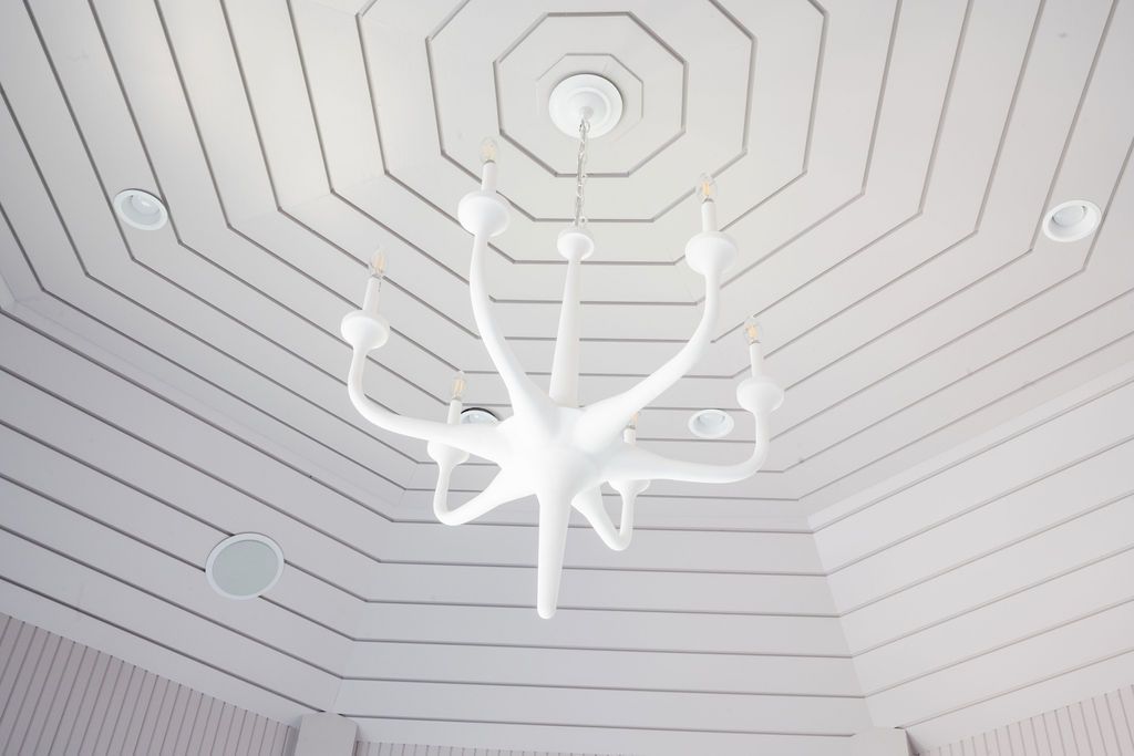 White modern chandelier hanging from a geometric white ceiling in a bright room