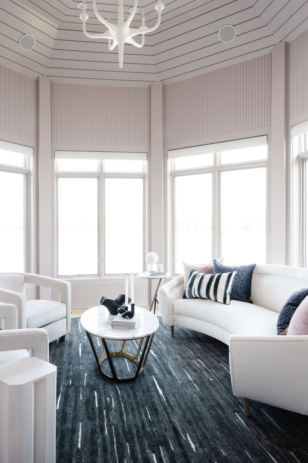 Bright white living room with curved windows, a dark rug, and a white sofa with blue pillows