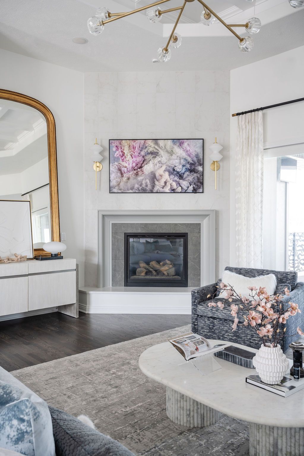 Modern living room with gray fireplace, floral armchair, gold mirror, and abstract wall art