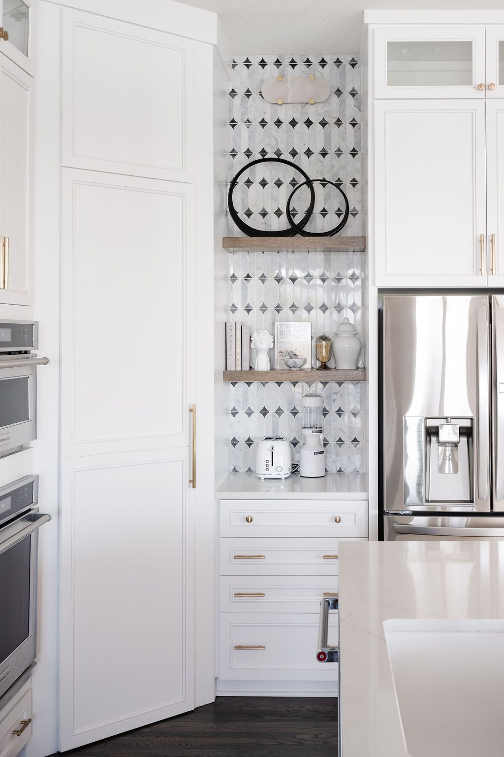 White kitchen nook with open shelves, black-and-white backsplash, and stainless steel refrigerator