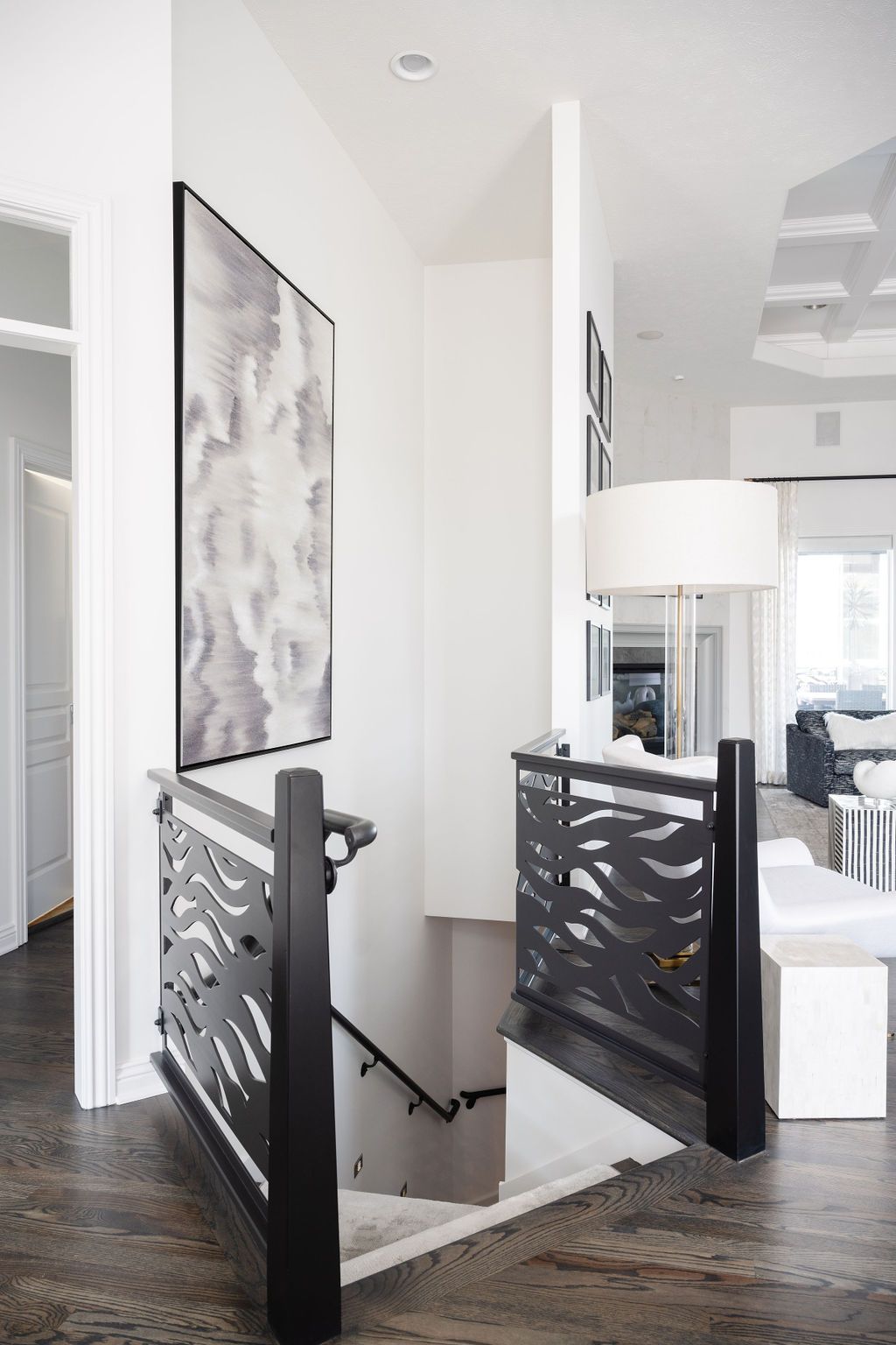 Bright modern staircase landing with black railing, white walls, and a floor lamp by a hallway.