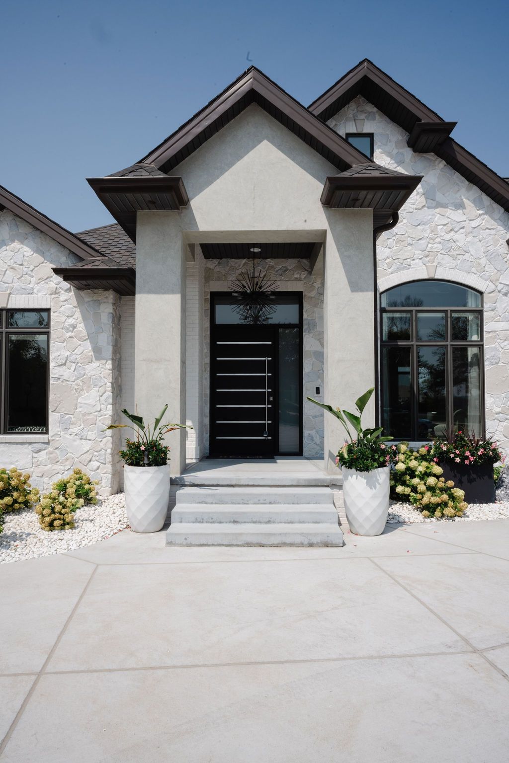 Modern white house exterior with black front door, stone steps, and potted plants
