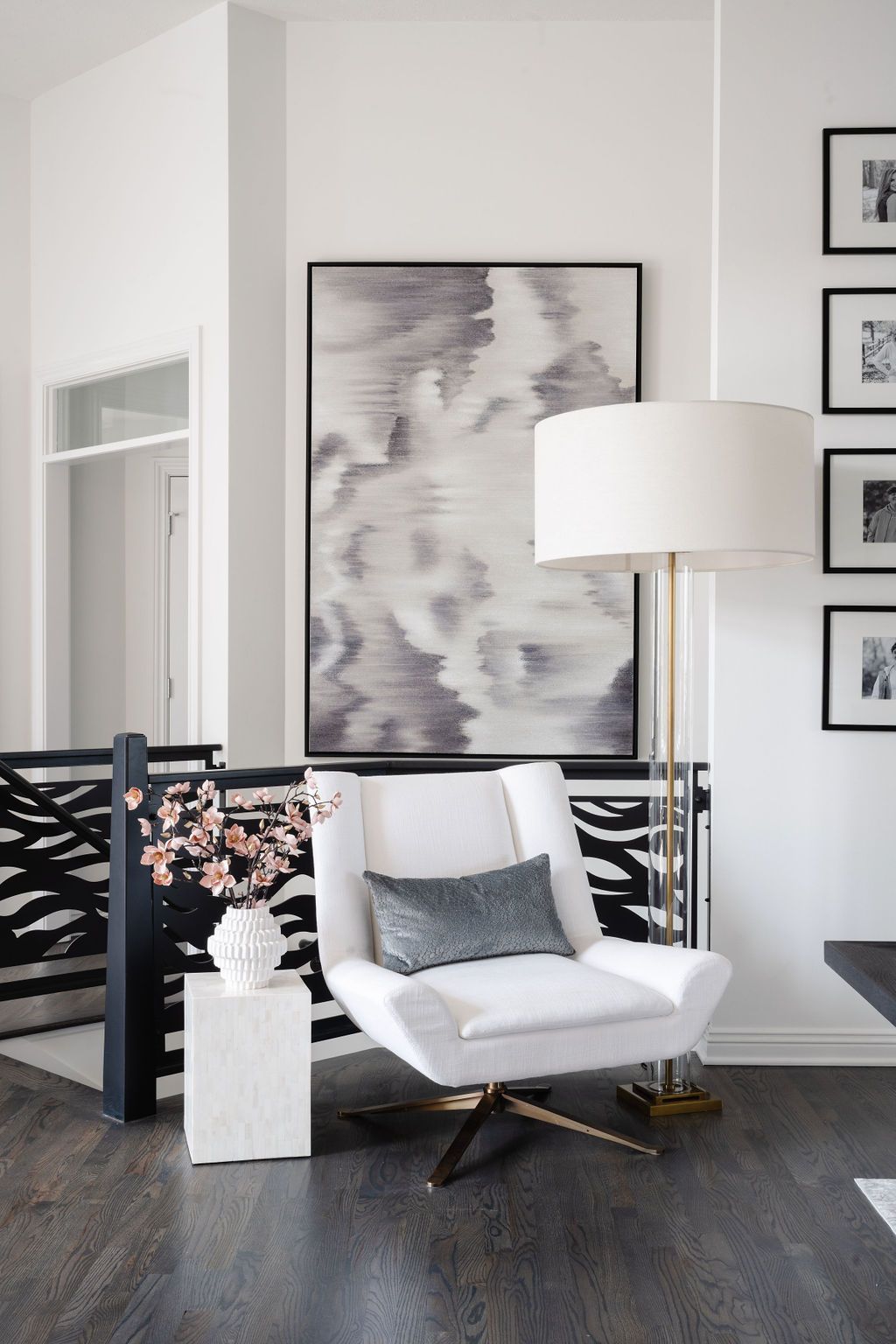 Modern living room with a white lounge chair, floor lamp, abstract art, and dark hardwood floors.