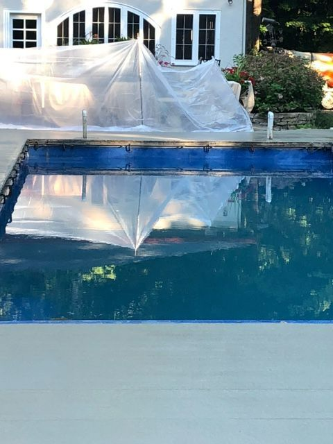 A large swimming pool is being painted blue in front of a house.