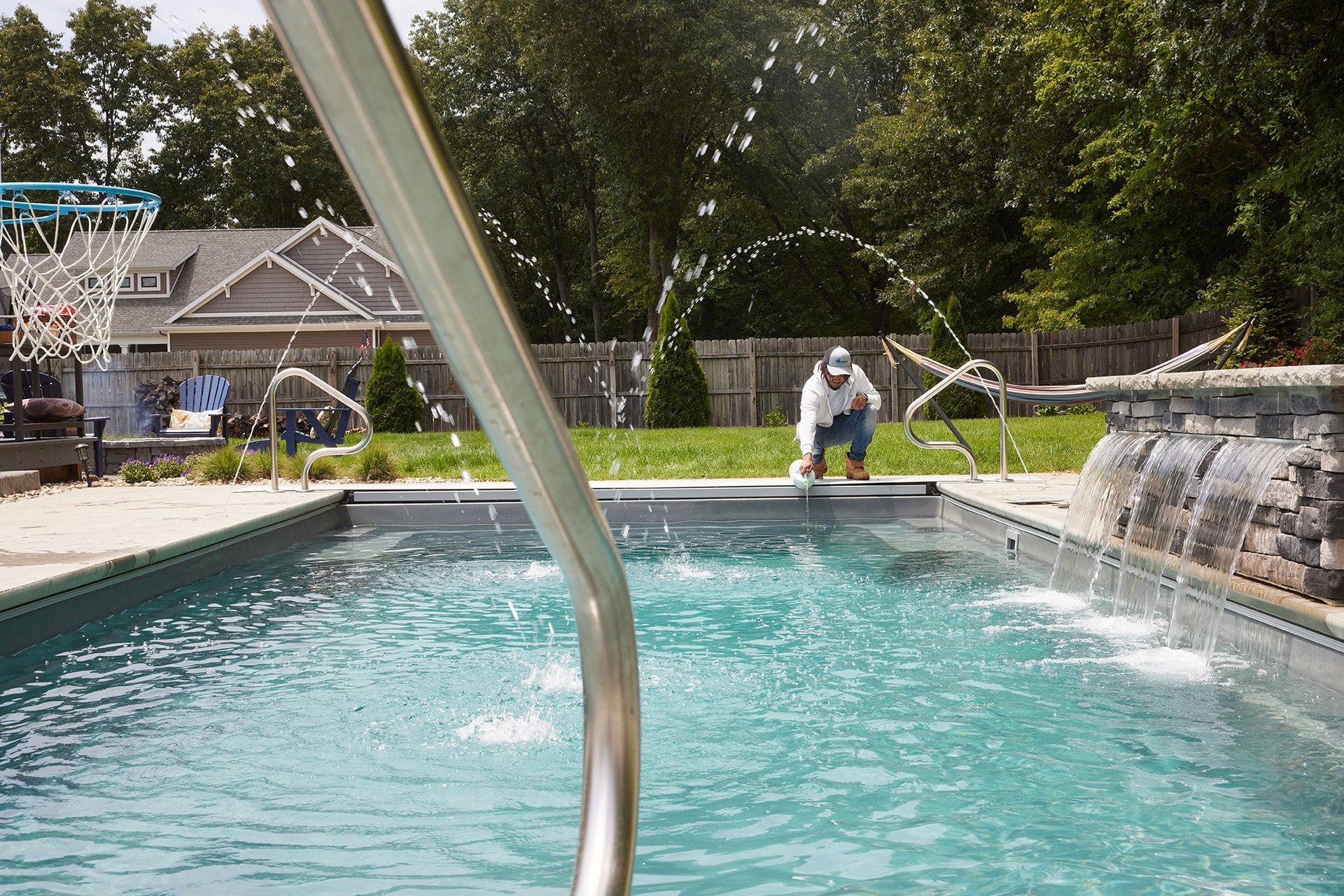 A man is kneeling on the edge of a swimming pool.