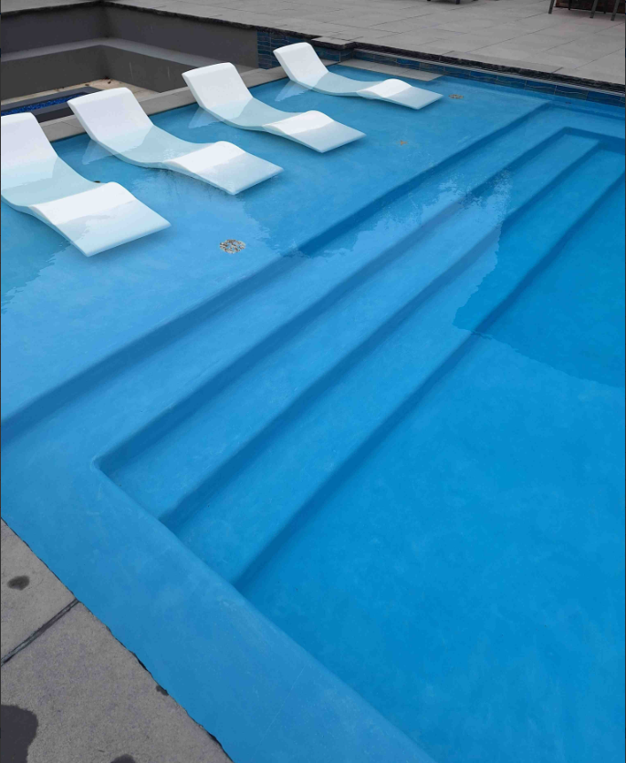 A swimming pool with blue water and white lounge chairs