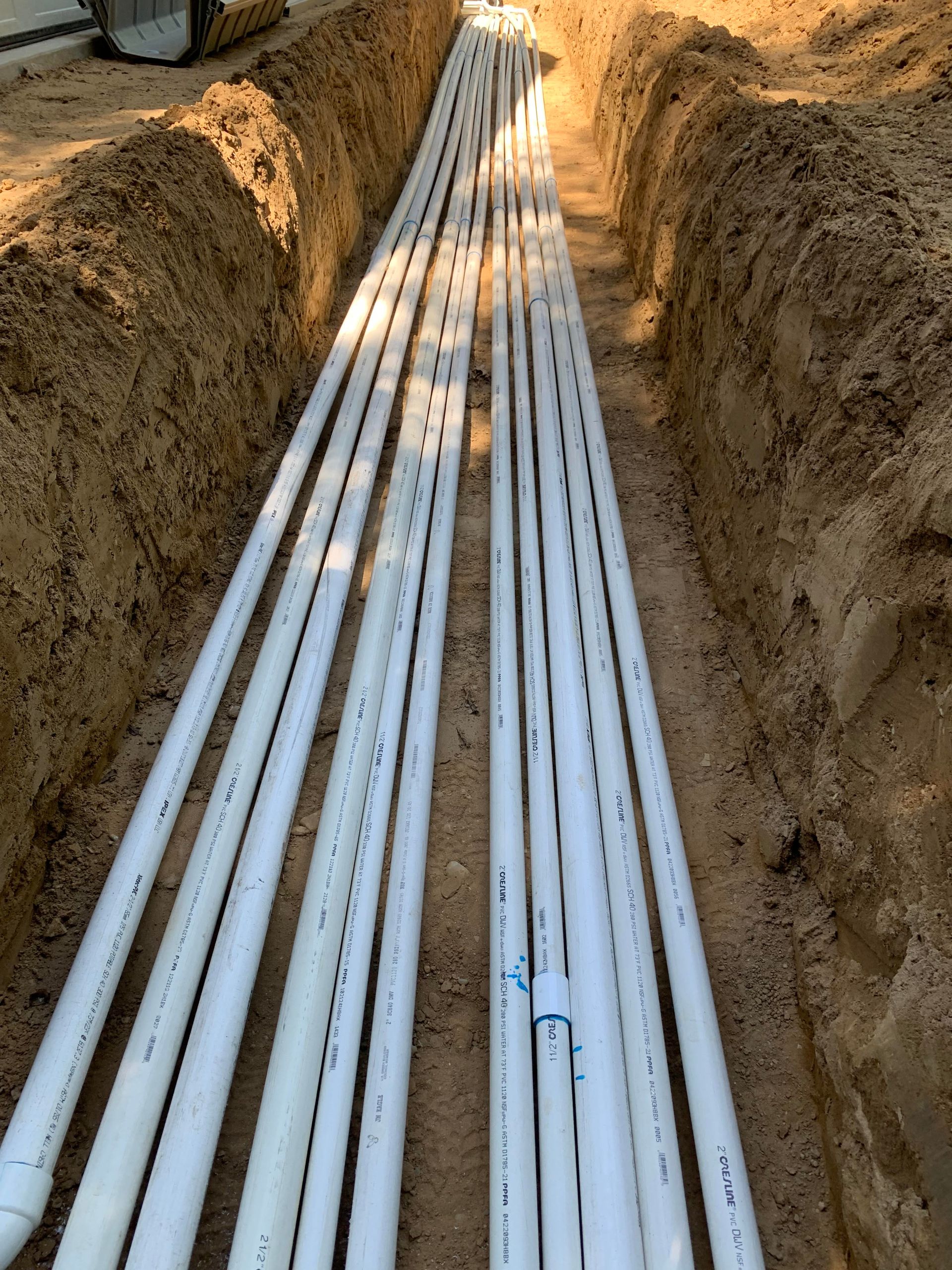 A bunch of white pipes are laying in the dirt.