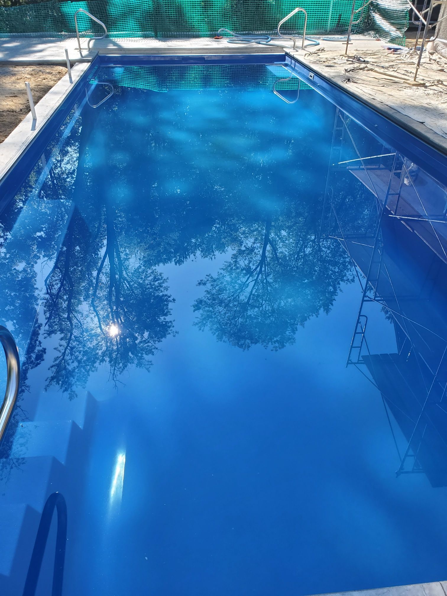 A large blue swimming pool with trees reflected in the water.