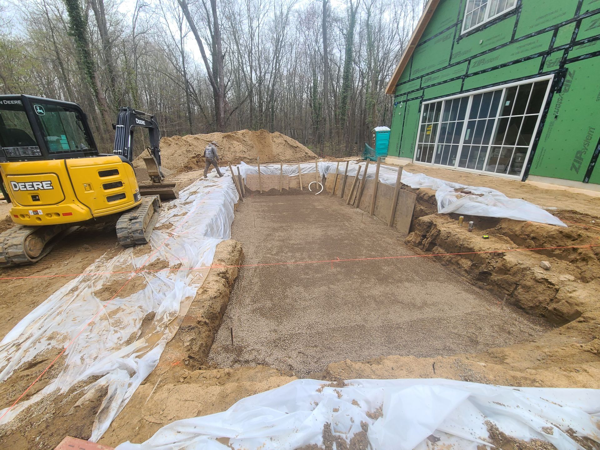 A yellow excavator is digging a hole in the ground in front of a house under construction.