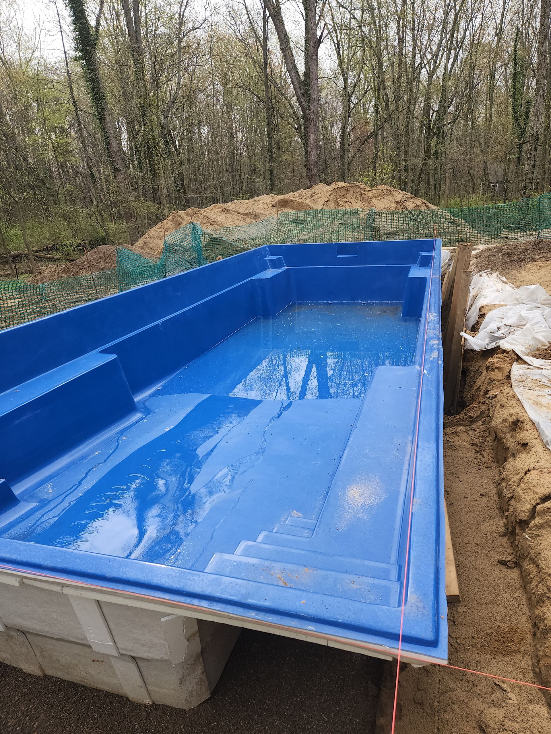 A blue swimming pool is being built in the woods.