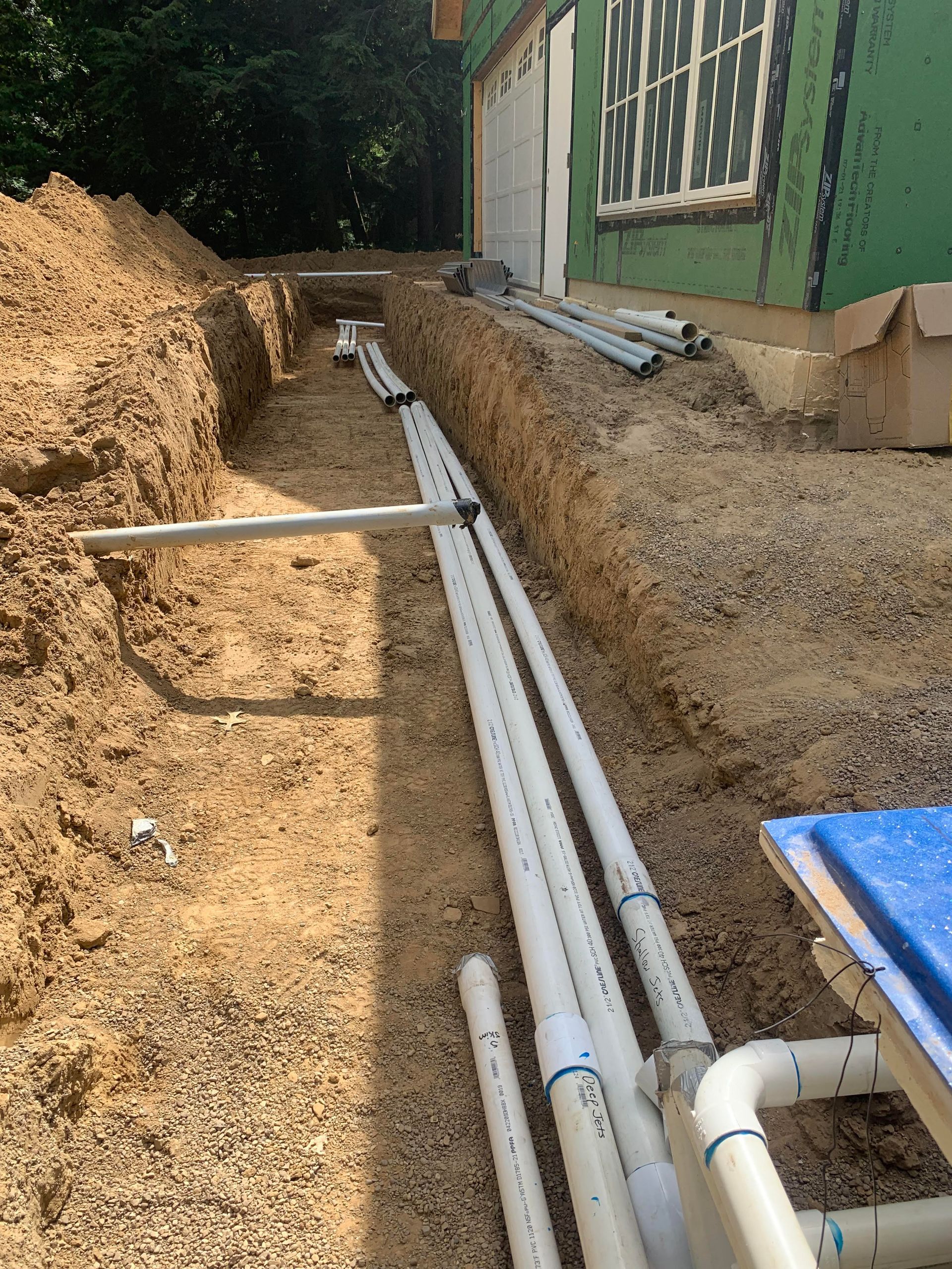 A bunch of pipes are being installed in a trench in front of a house.