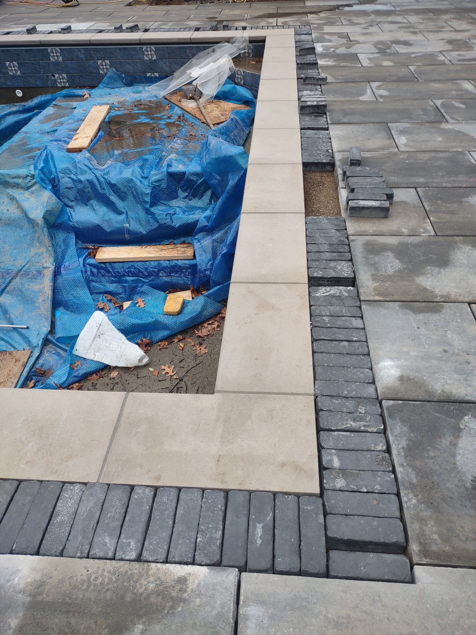 A brick walkway is being built around a pool.