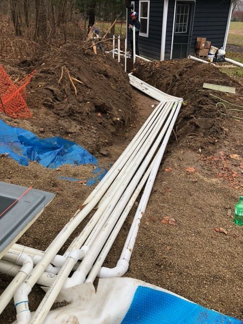 A bunch of pipes are laying in the dirt in front of a house.