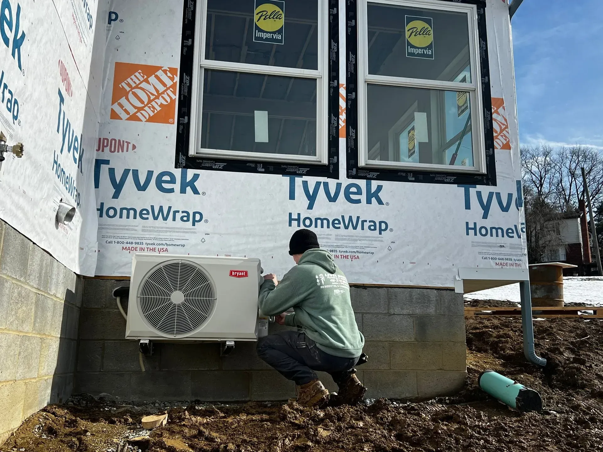 Person installing an AC unit on the exterior wall of a new house under construction.