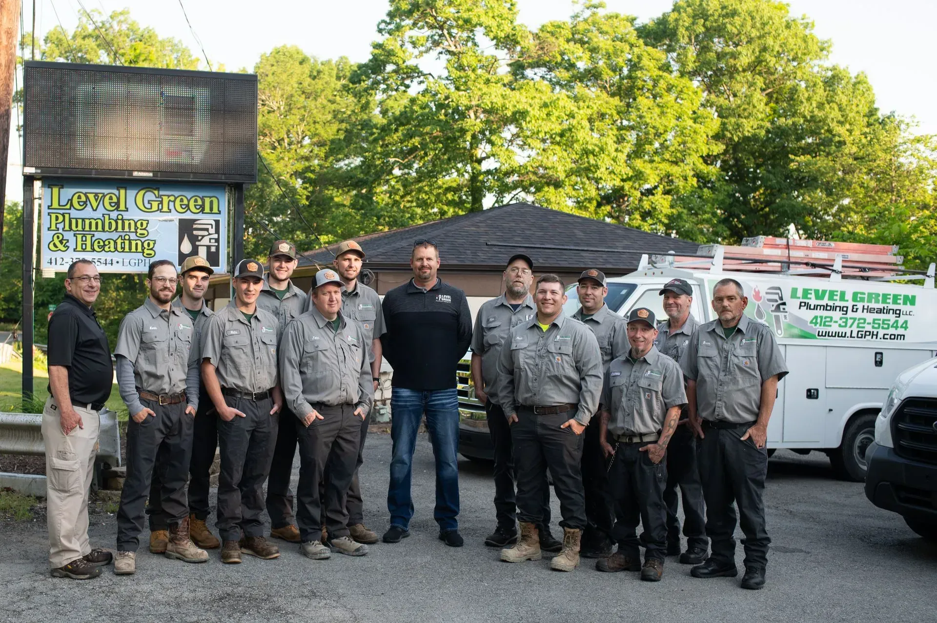 Group of men in work uniforms stand in front of a building and trucks.