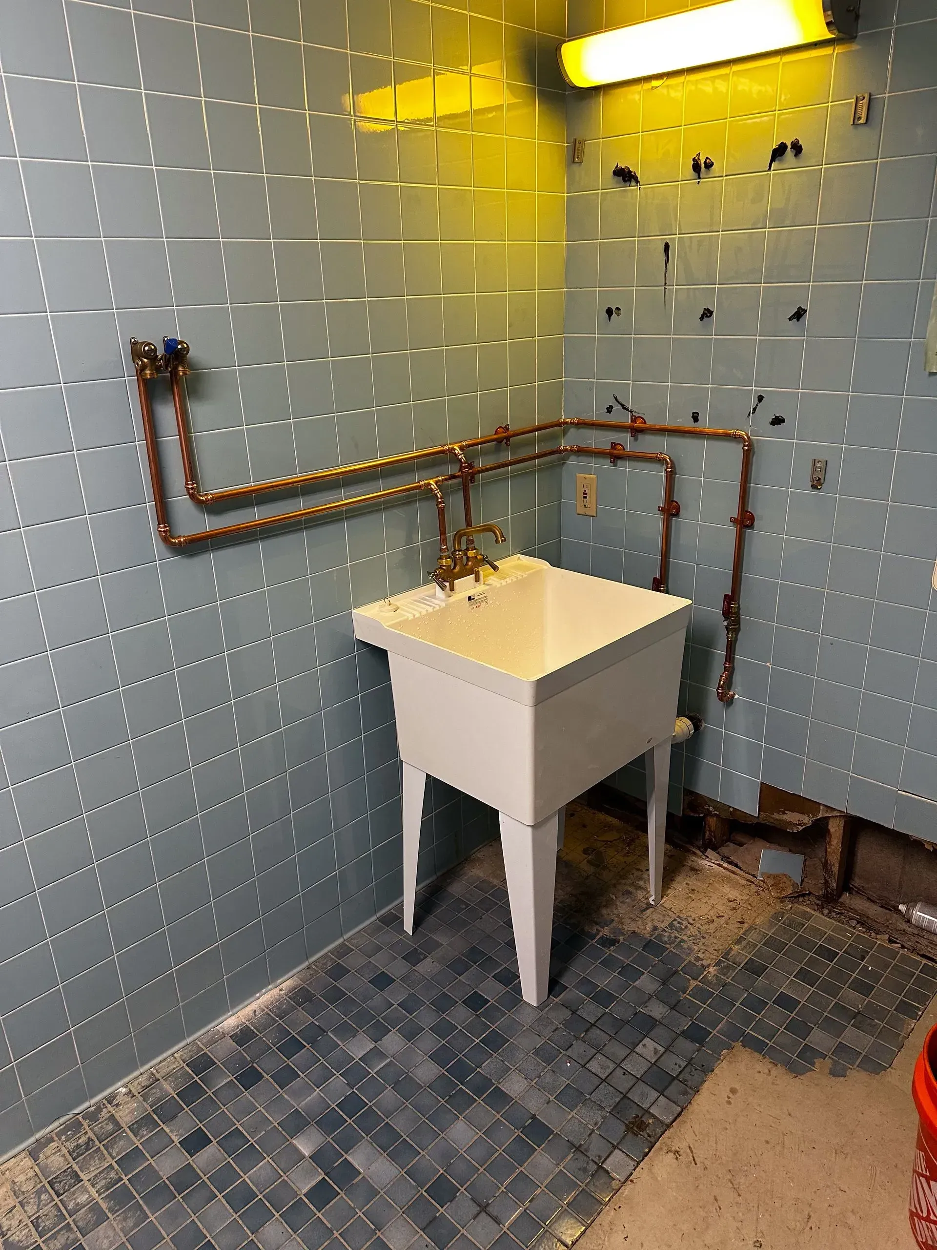 Laundry room with a white utility sink, copper pipes, and blue tile walls.