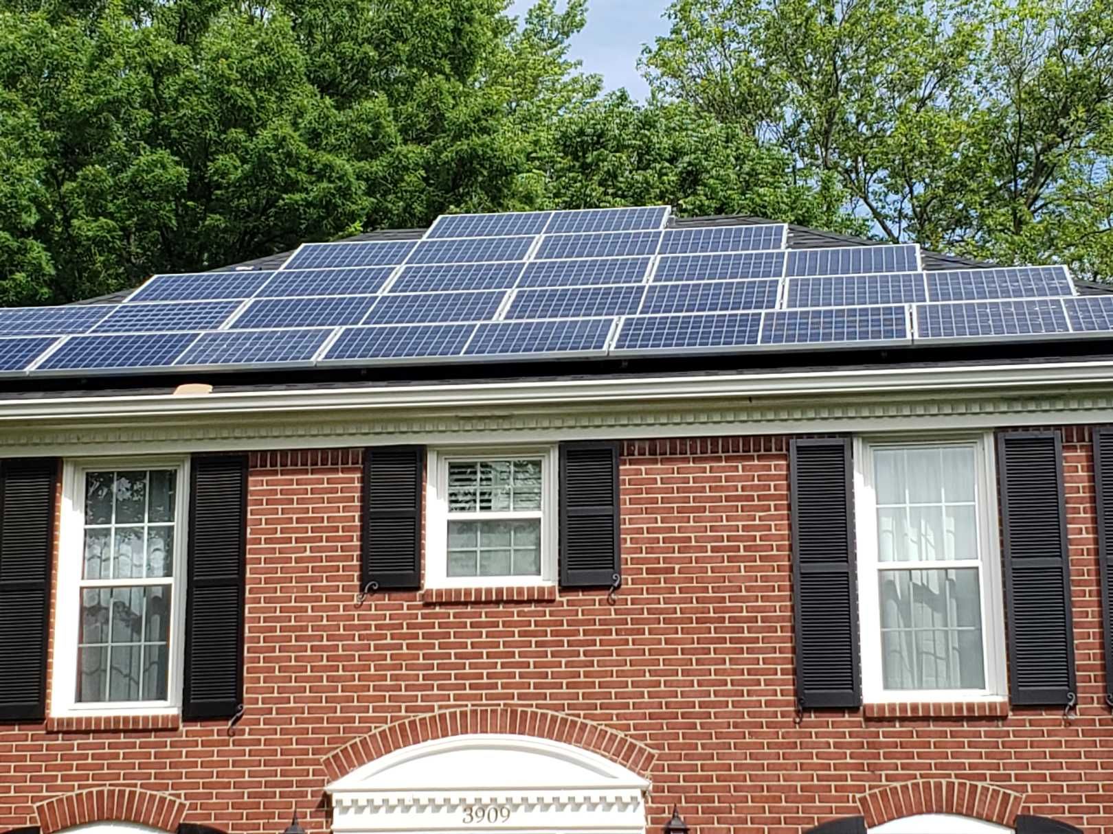 A brick house with black shutters and solar panels on the roof.