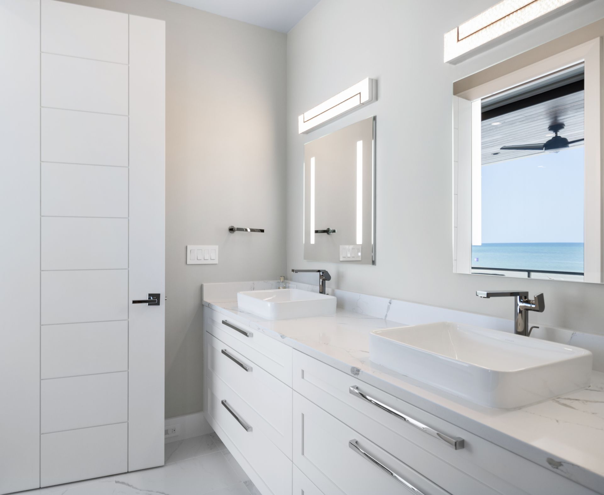 A bathroom with two sinks and a window overlooking the ocean