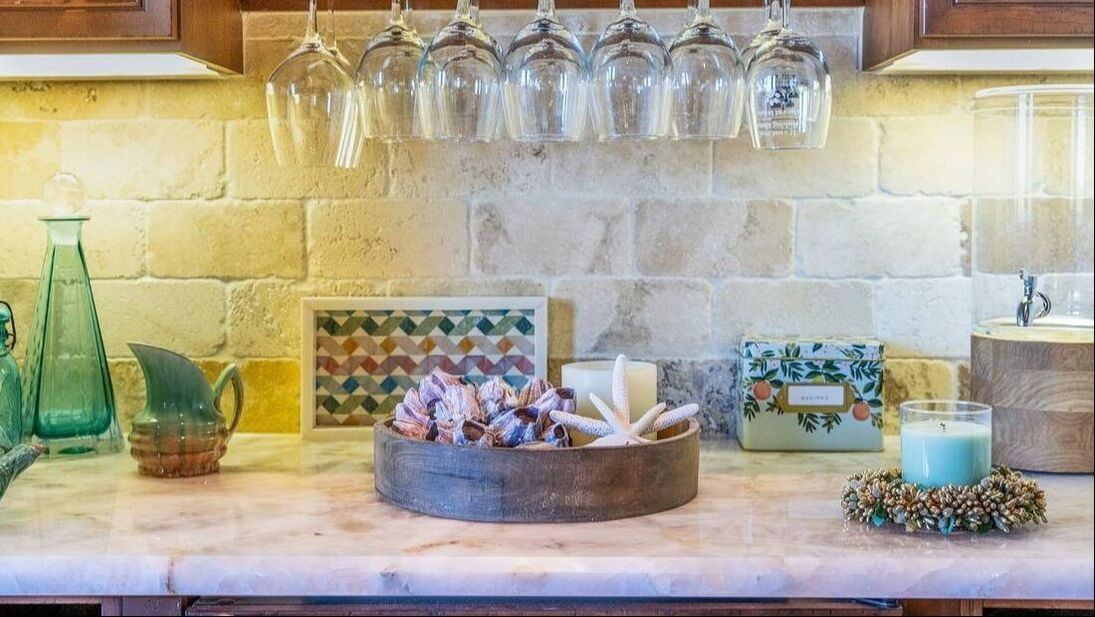 a kitchen counter with a tray of seashells and wine glasses hanging on the wall .