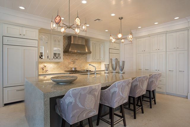 a kitchen with white cabinets , granite counter tops , stools and a large island .