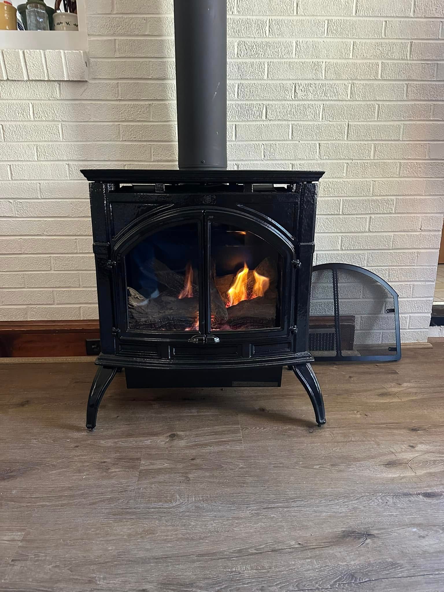 Black cast iron wood-burning stove with flames, in front of a white brick wall.